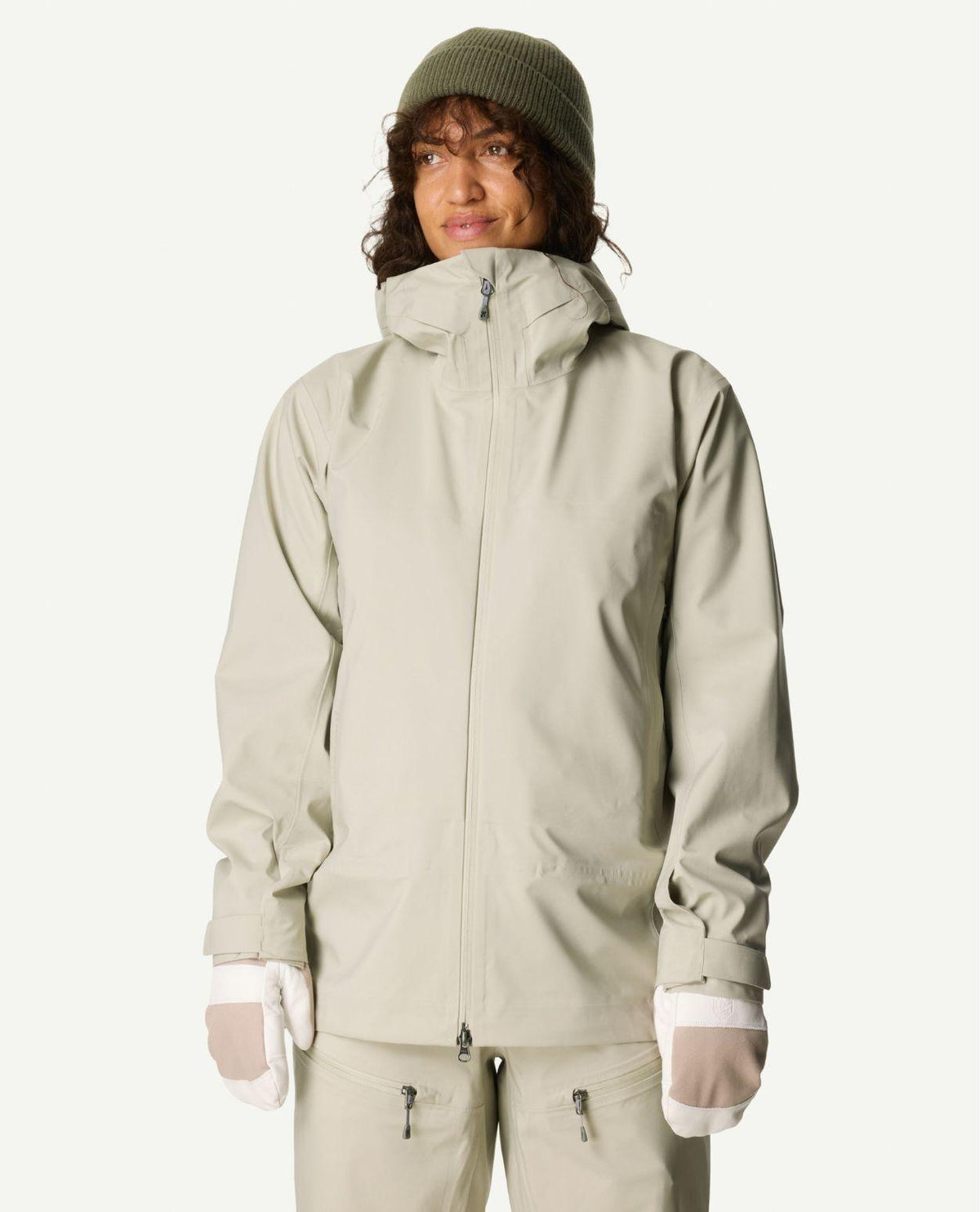 Kvinna iklädd Houdini Ride Jacket II i färgen greenish gray samt matchande byxor, mössa och vantar.