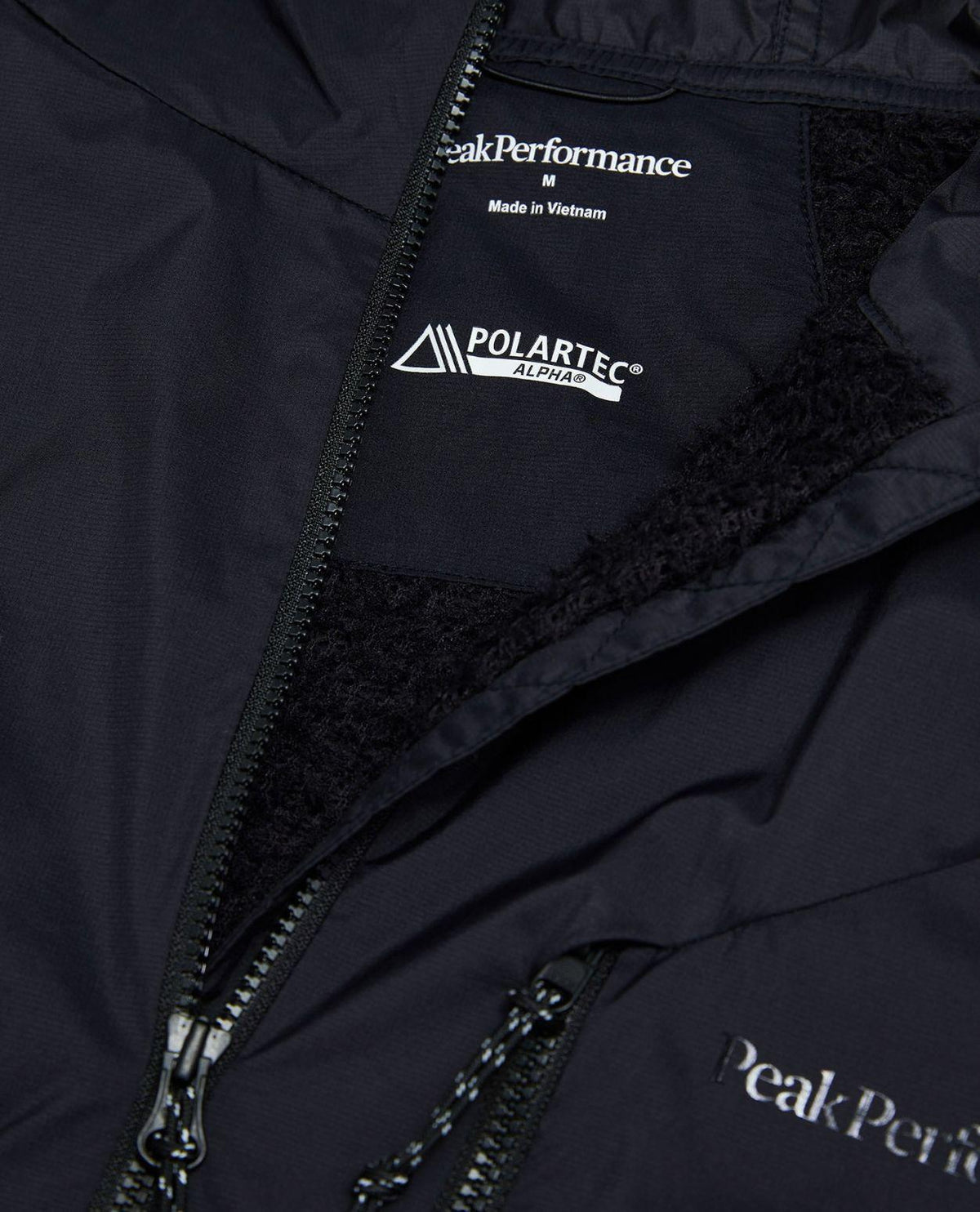 Närbild på insidan, logotypen och Polartec Alpha-detaljen på Peak Performance Freelight Alpha Jacket Men i svart.