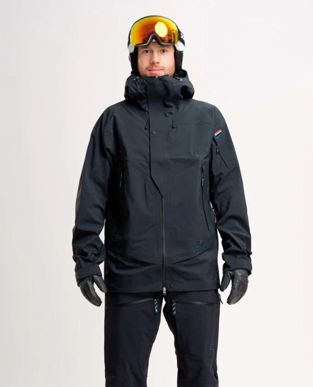 Manlig skidåkare iklädd mörkblå Elevenate Pure Jacket med tillhörande skidbyxor, hjälm och skidglasögon.