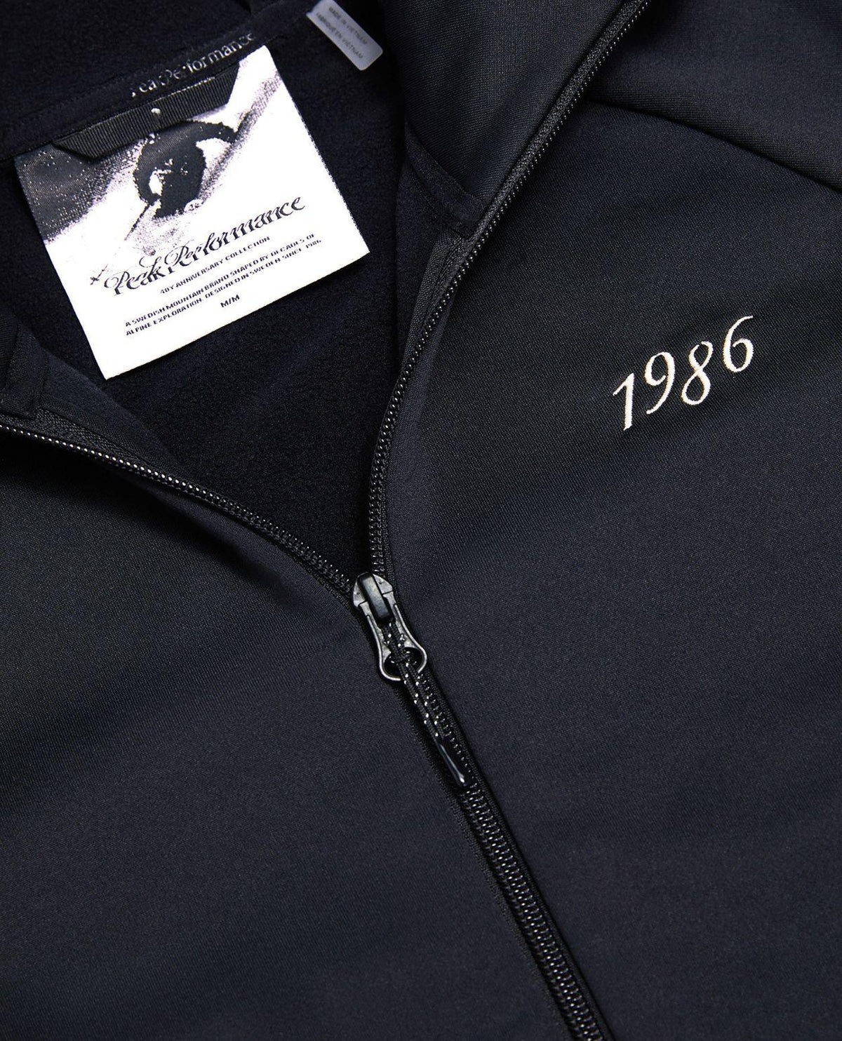 Peak Performance 40Y Rider Zip Hood i svart med jubileumsetikett och tryckt årstal 1986.