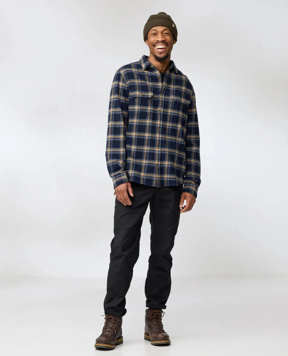 Man som bär Fjällräven Övik Heavy Flannel Shirt i mörkblått och brunt med svarta byxor.