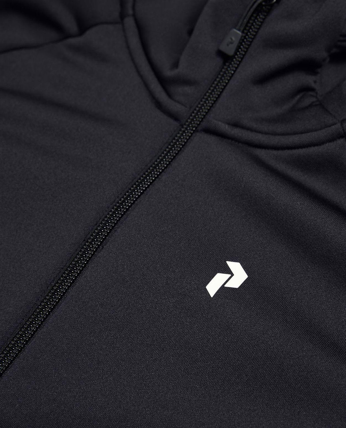 Närbild på Peak Performance Rider Essentials Zip Hood Junior i svart med dragkedja och vit logotyp.