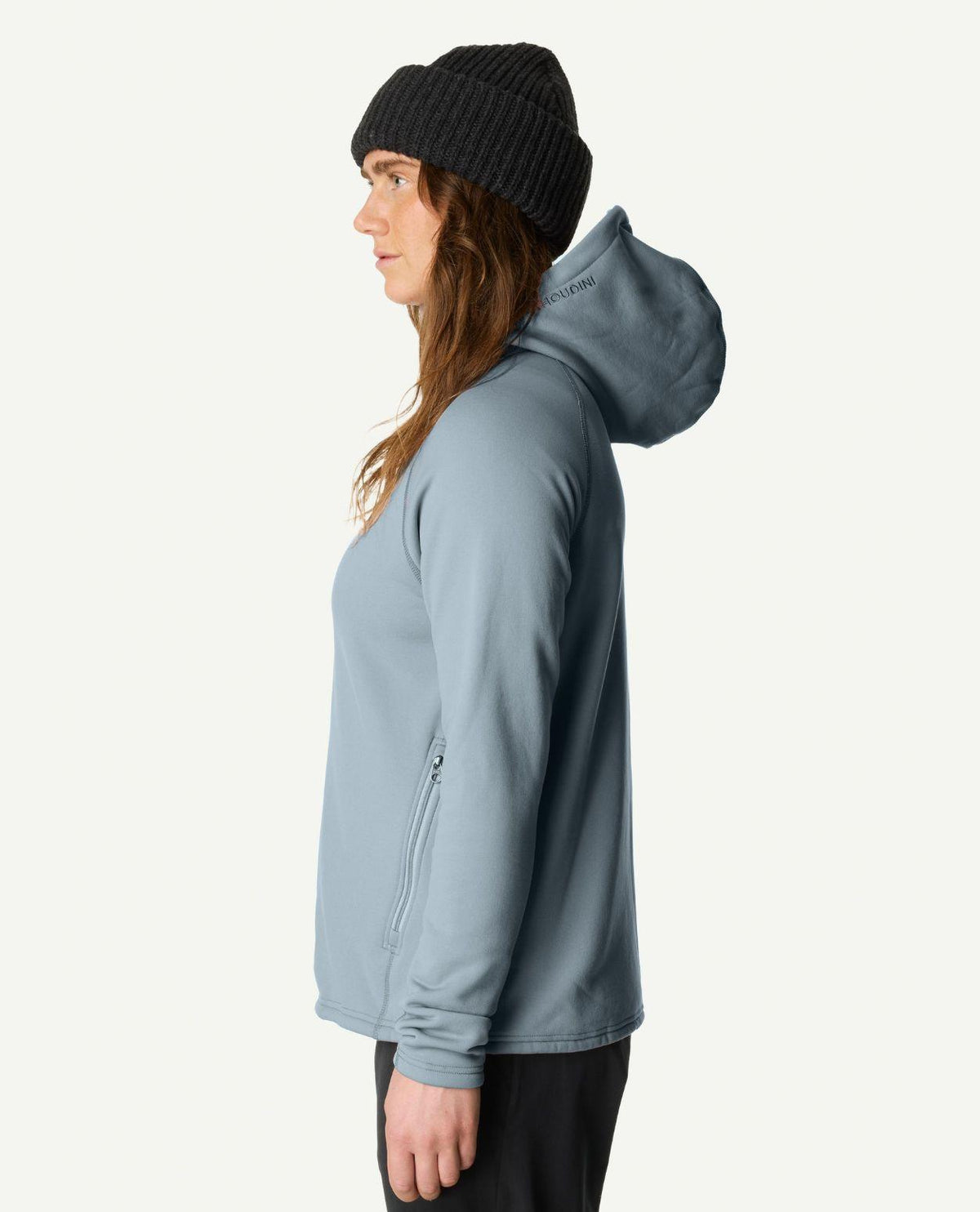 Kvinna i profil som bär Houdini Power Up Houdi i färgen brink blue och en svart mössa.