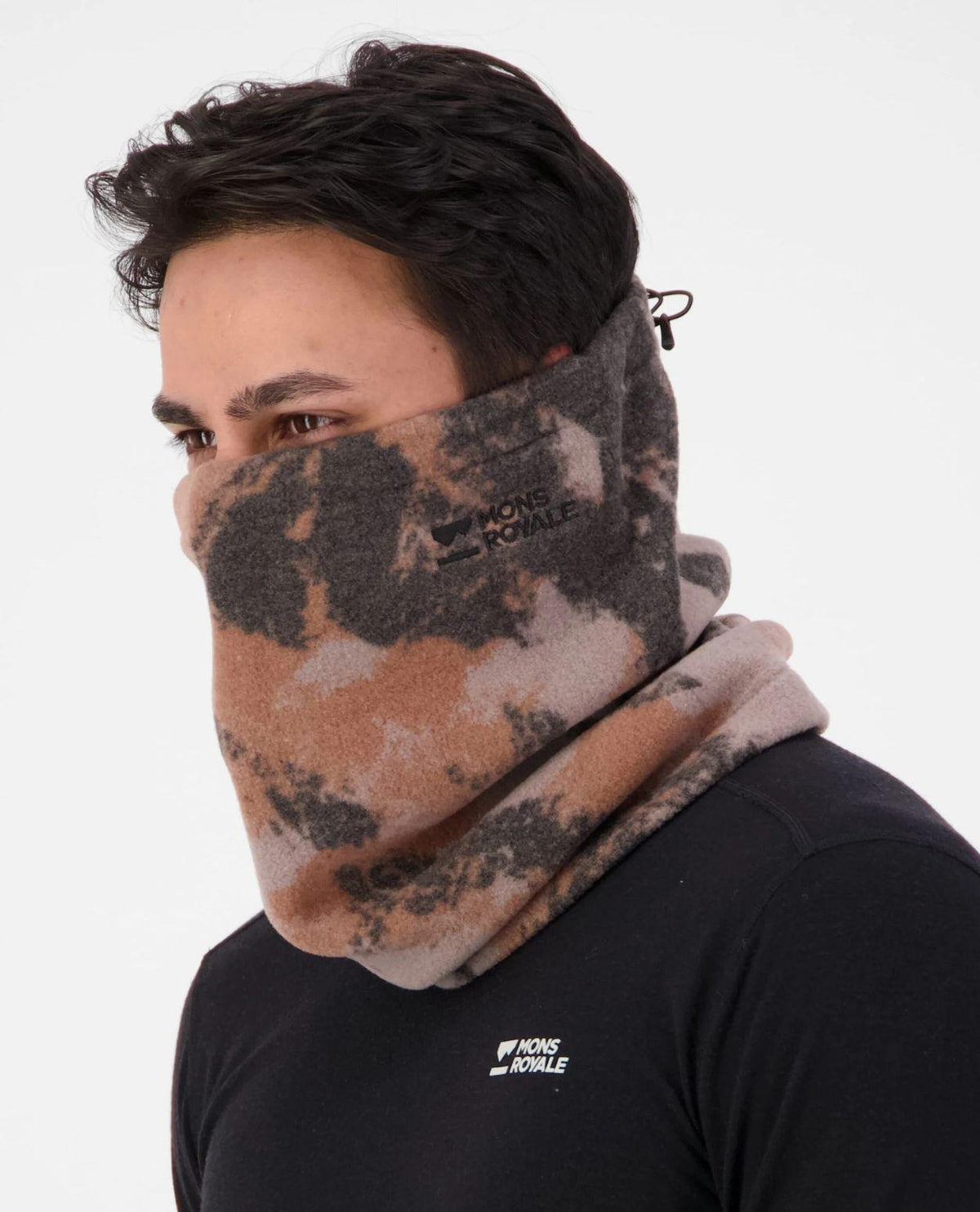 Person bär Mons Royale Pileup Fleece Neck i orange kamouflagemönstrad fleece runt halsen.