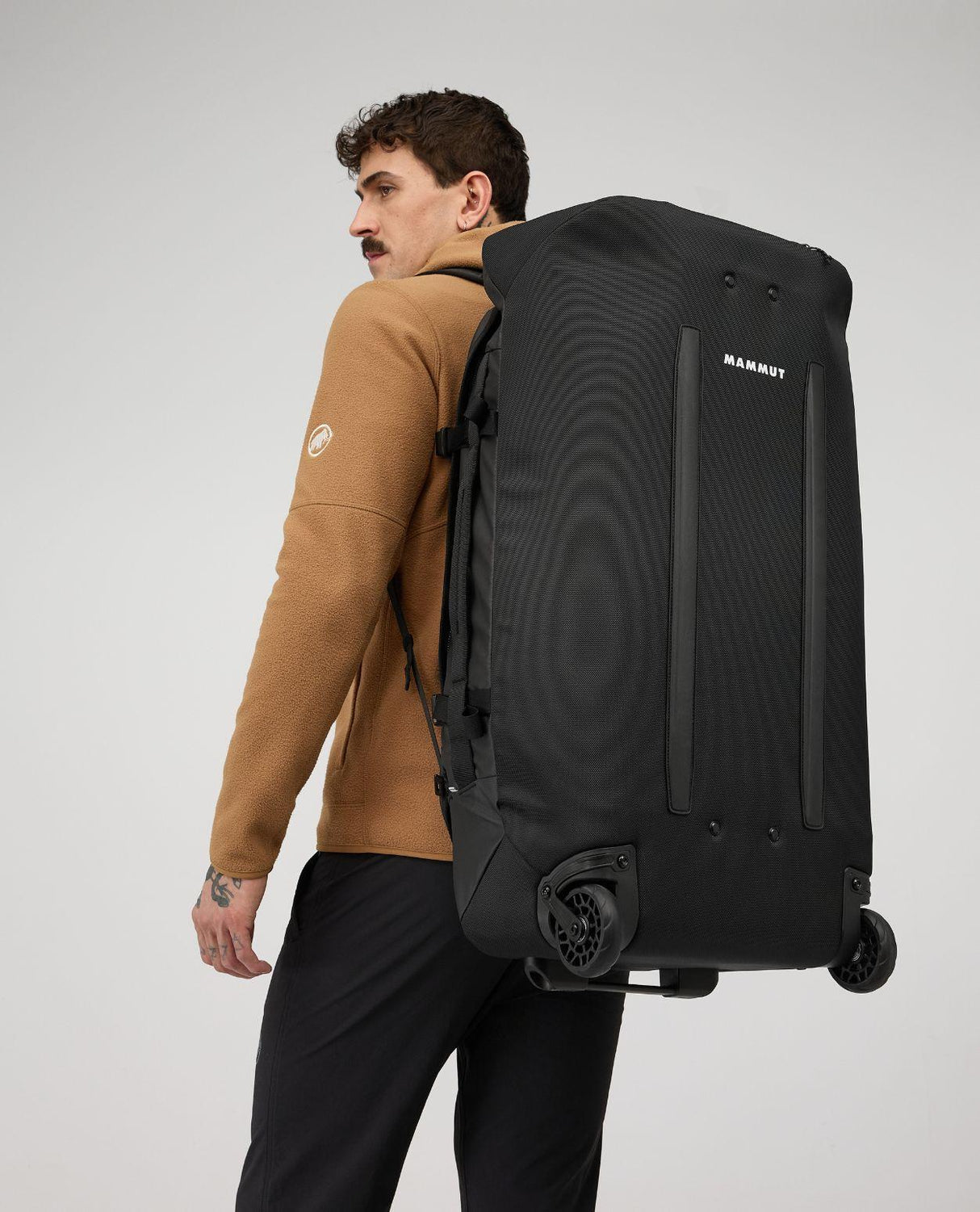 Person som bär den svarta resväskan Mammut Wheeled Cargo 90 på ryggen med synliga hjul.