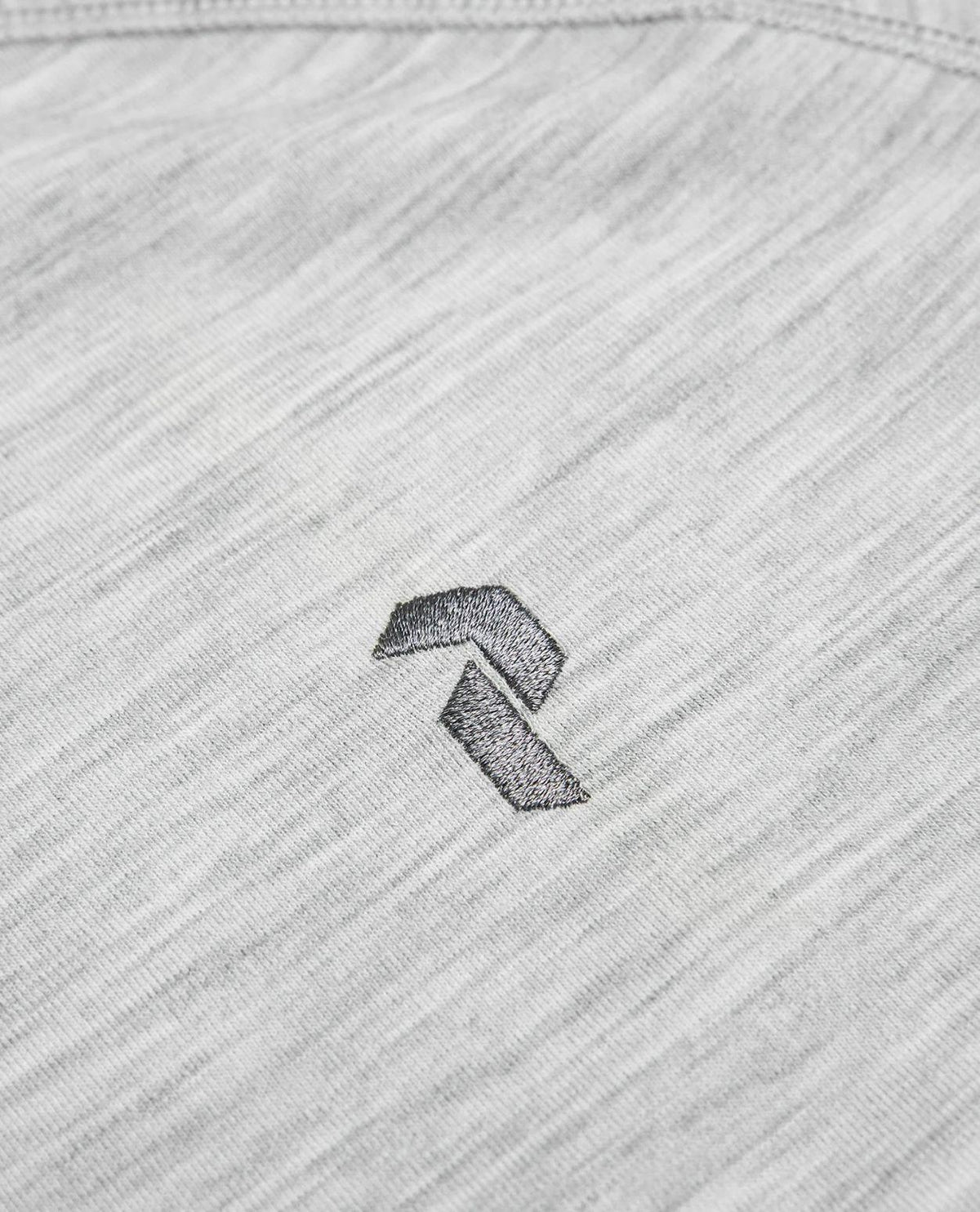 Närbild på det gråmelerade tyget med en broderad Peak Performance-logotyp.
