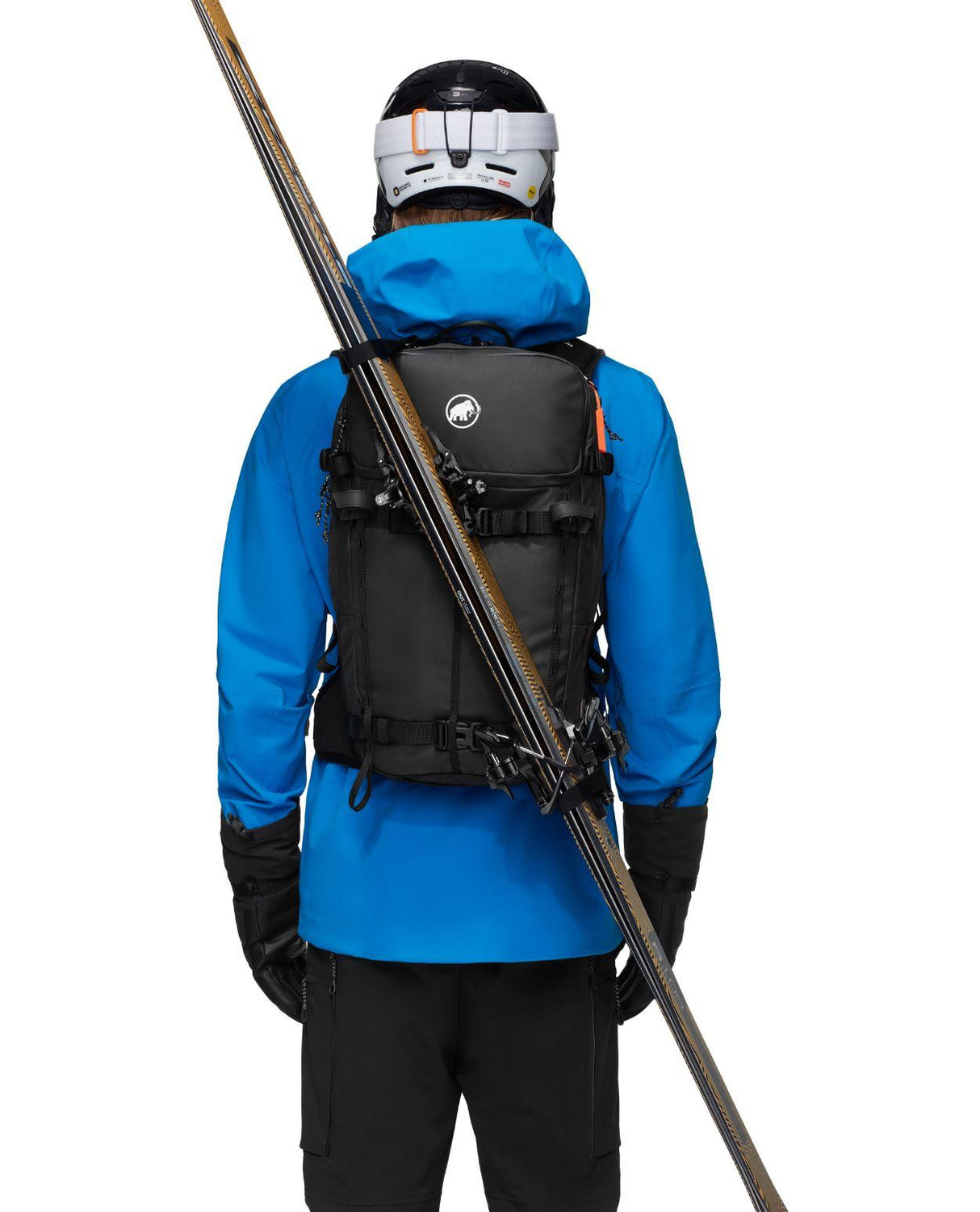 Skidåkare i blå jacka bär en svart Mammut Nirvana 22 ryggsäck med skidorna fästa diagonalt på ryggen.