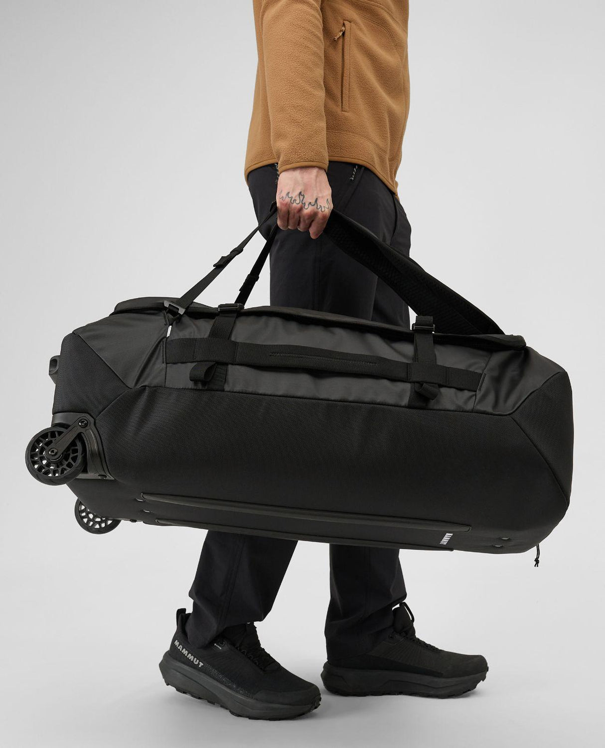 Mammut Wheeled Cargo 90 i svart buren av person som visar väskans robusta hjul och handtag.