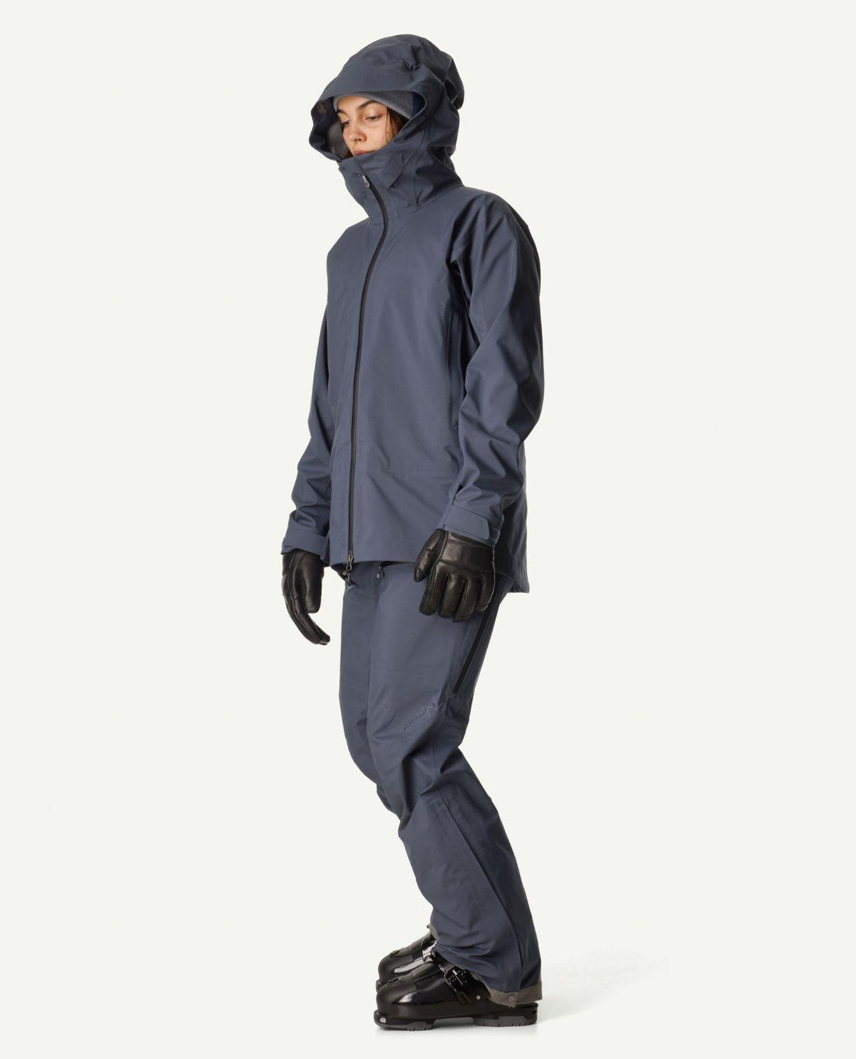 Kvinna iklädd Houdini Ride Jacket II i blått med matchande byxor, skidhandskar och pjäxor.
