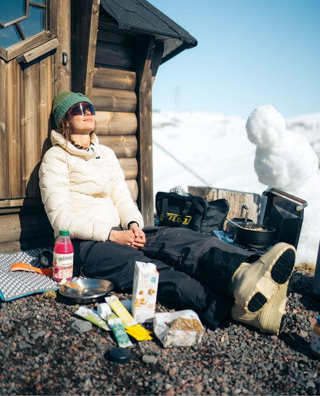 Skidåkare som njuter i solen mot en trävägg iklädd FUBUKI Niseko 3.0 Low vinterkängor i sandfärg.