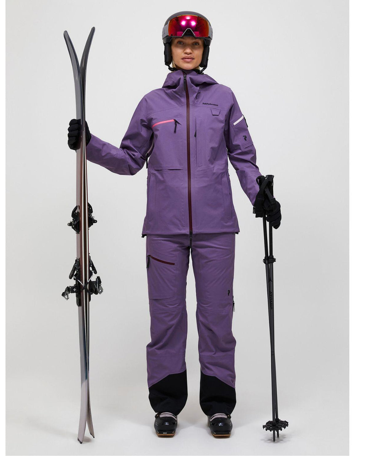 Skidåkare i lila Peak Performance Alpine Gore-Tex 3L Jacka och matchande skidbyxor håller i skidor och stavar.