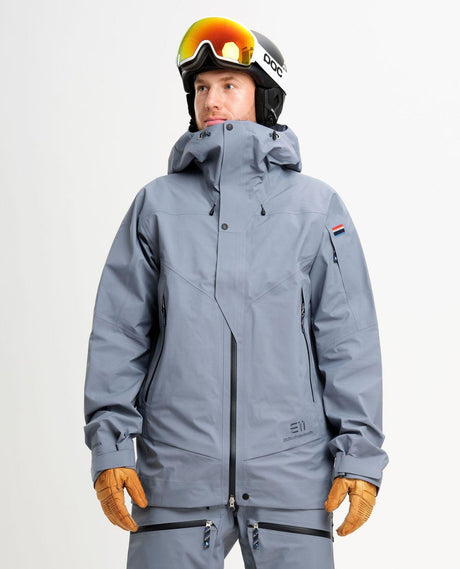 Manlig skidåkare iförd Elevenate Pure Jacket i blått med matchande skidkläder, hjälm och skidglasögon.