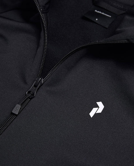 Närbild på dragkedja och bröstlogotyp på svart Peak Performance Rider Essentials Zip Jacket för dam.