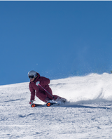 Kvinna i röd skidoutfit som carving-svänger i pisten med Blizzard Phoenix-skidor i strålande sol.