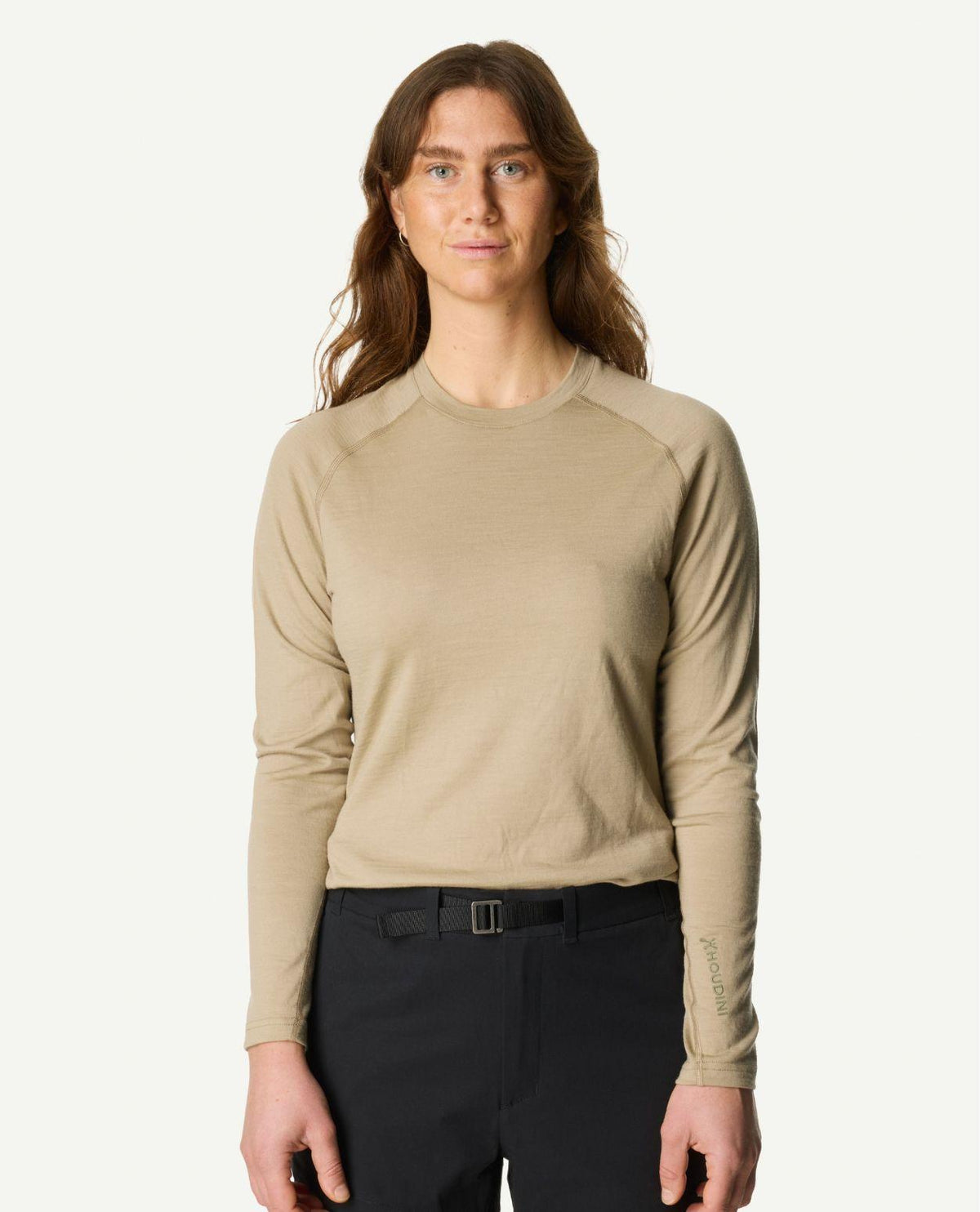 En kvinna iklädd Houdini Puremerino Crew underställströja i färgen powder green och svarta byxor.