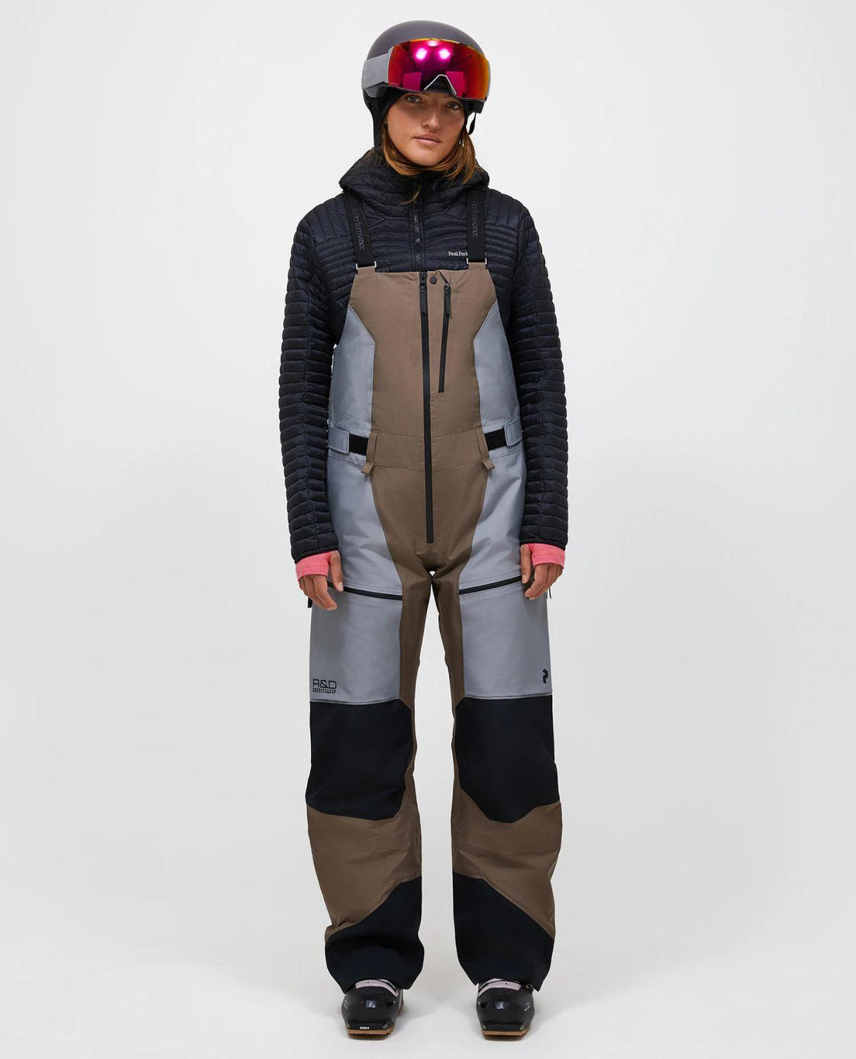 Skidåkare i dammodellens Peak Performance Vertical Gore-Tex Pro Bib Pants i färgen Terrain Tan och ljusgrå framifrån.