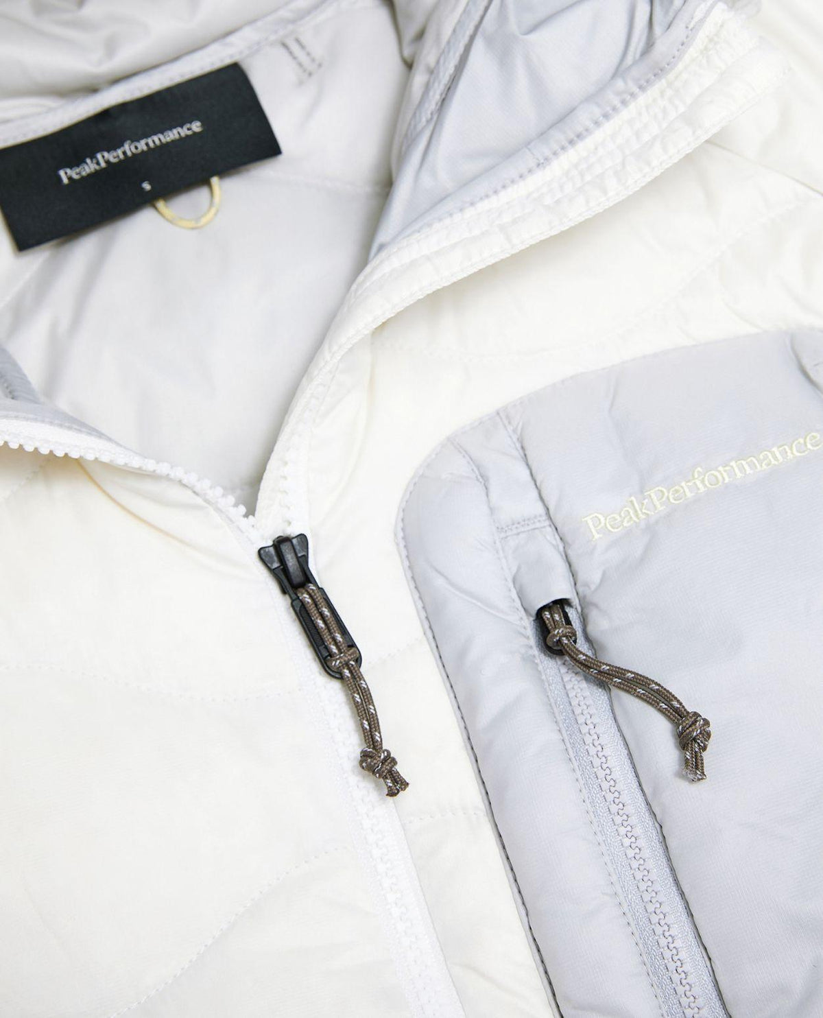 Närbild på Peak Performance Helium Utility Down Hood Jacket Dam i offwhite och antarktisgrå med dragkedja.