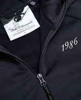 Närbild på den svarta Peak Performance 40Y Rider Zip Hood dam med dragkedja och broderat årtal.