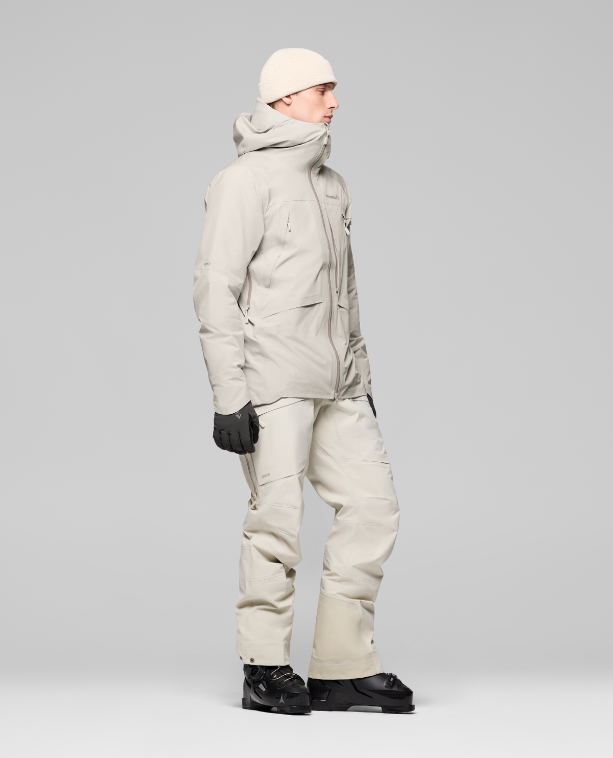 Norrøna Møre Gore-Tex Jacket Men i färgen Oatmeal, visad från sidan med matchande skidbyxor och pjäxor för herrar.