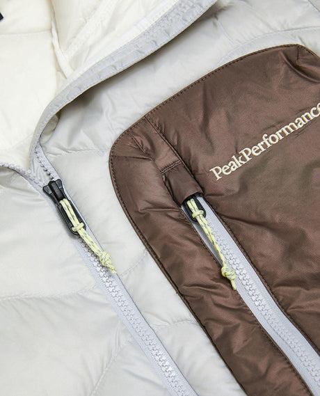 Närbild på bröstficka och dragkedja på Peak Performance Helium Utility Down Hood Jacket i färgerna Antarctica och Terrain Tan.