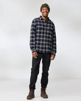 Man som bär Fjällräven Övik Heavy Flannel Shirt i mörkblått och brunt med svarta byxor.