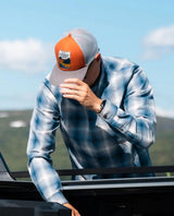 Person i en blårutig skjorta bär Elevenate Tofino Cap i färgen copper utomhus i ett naturlandskap.