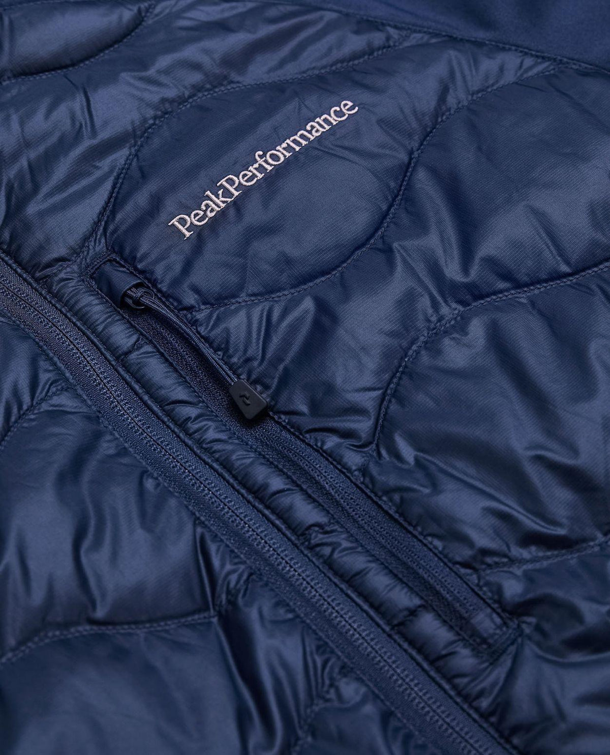 Närbild på Peak Performance Helium Down Hybrid Jacket i blått som visar bröstficka och logotyp.