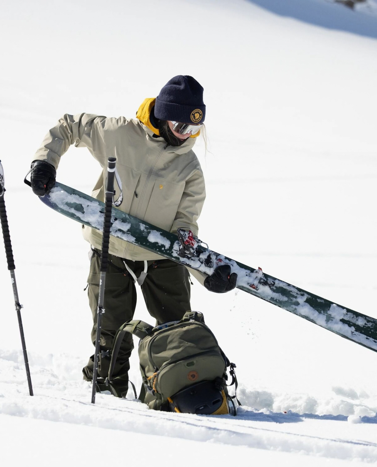 Skidåkare i snöigt fjällandskap som förbereder utrustning för toppturen med skidor och stavar.