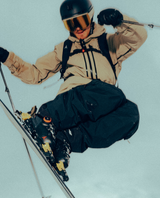 Alpinskidåkare i luften med Atomic Hawx Prime 130 S BOA pjäxor, beige skaljacka och svarta skidbyxor.