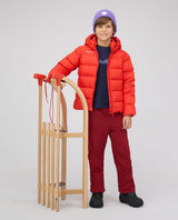 Barn i röd Mammut Waymarker IN Hooded Jacket Junior som står bredvid en träkälke.