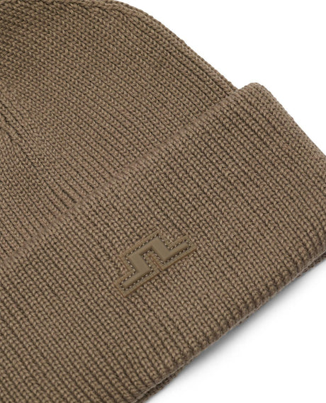 Närbild på den bruna mössan J.Lindeberg Vale Beanie med tydlig logotyp på uppvikt kant.