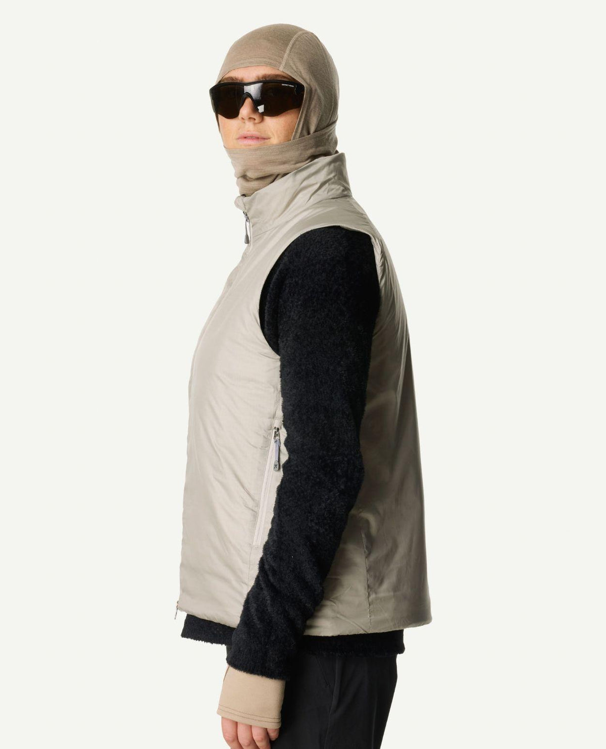 En person i profil som bär Houdini Dunfri Vest i färgen sandstorm över en svart tröja.