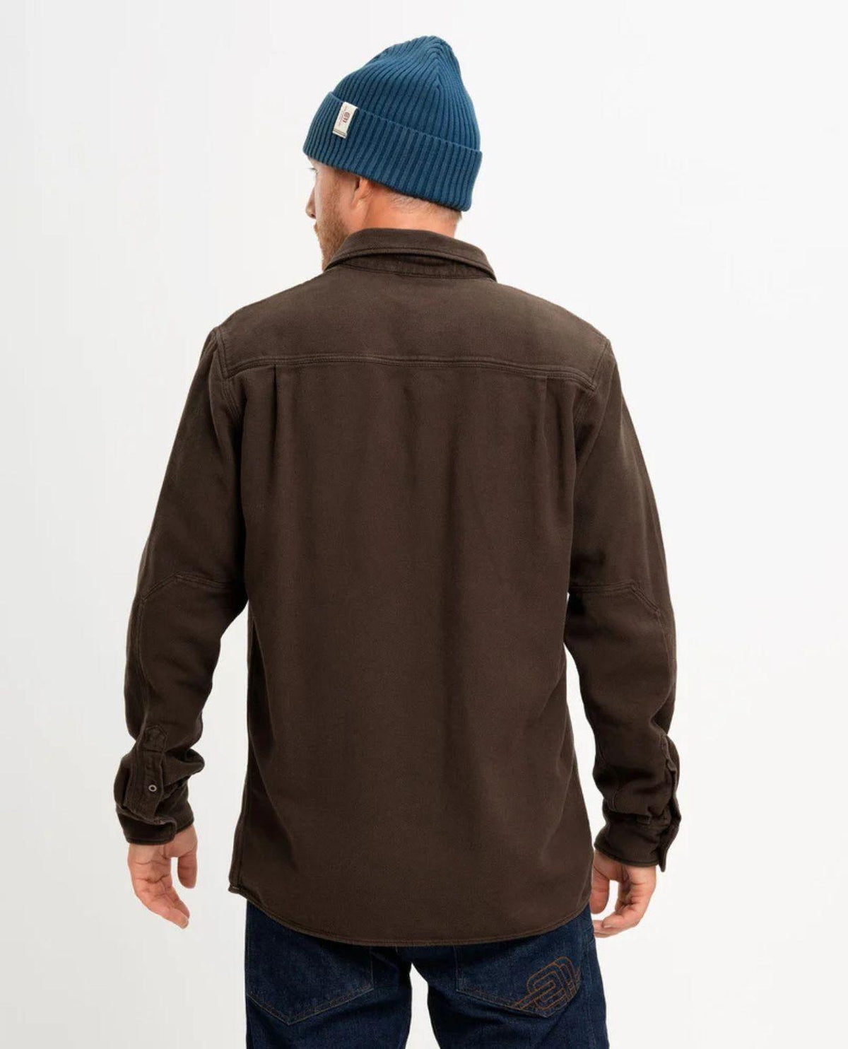 Elevenate Hokkaido Shirt Men i färgen Shiitake Brown sett bakifrån, med en person som bär den bruna bomullsskjortan tillsammans med mörkblå mössa och jeans.
