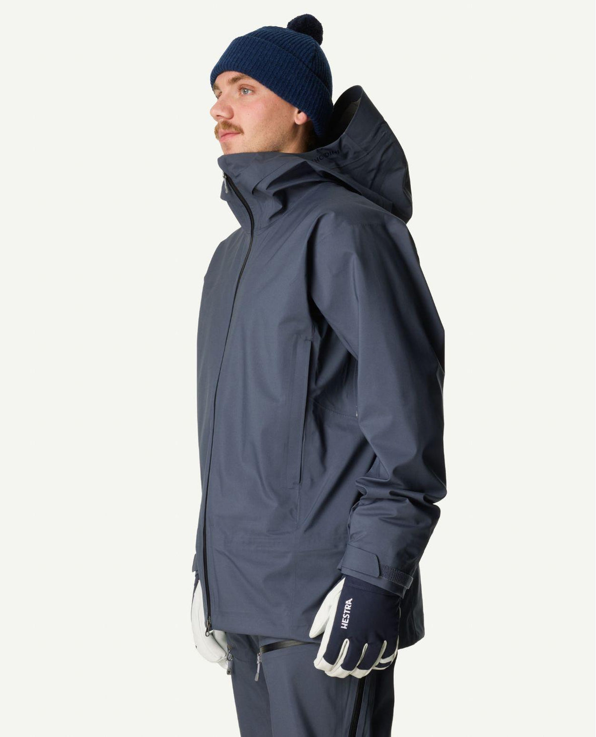 Manlig skidåkare bär Houdini Ride Jacket II i blått och matchande mössa från sidan.