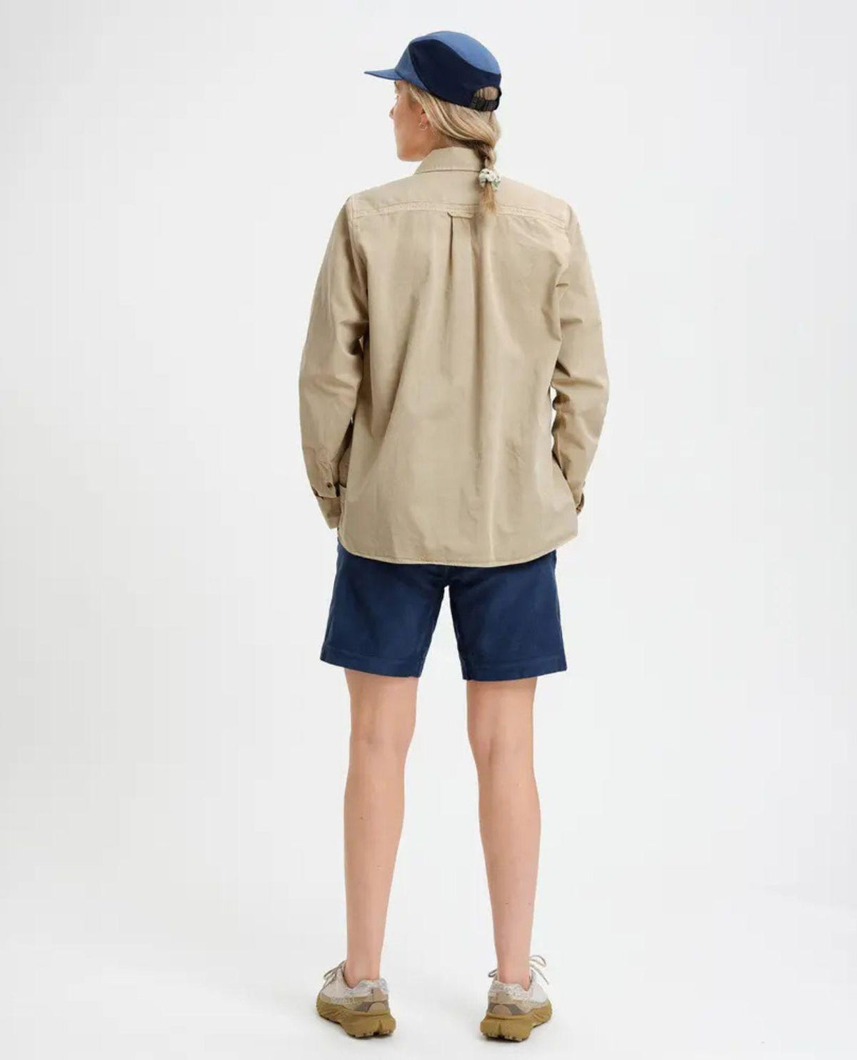 Kvinna sedifrån iförd Elevenate Utility Shirt i safari-beige färg tillsammans med blå shorts.