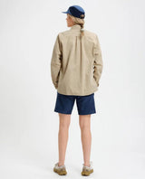 Kvinna sedifrån iförd Elevenate Utility Shirt i safari-beige färg tillsammans med blå shorts.