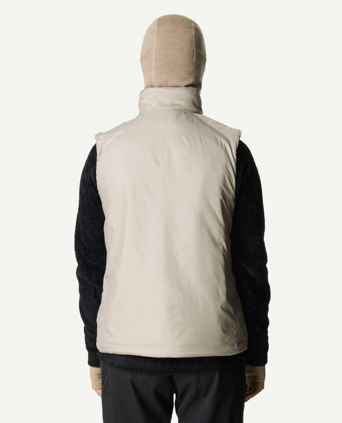 Kvinna bakifrån som bär en beige dunjacka väst och huva.