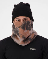 Person bär Mons Royale Pileup Fleece Neck i Mtn Camo Orange samt en svart mössa och tröja.