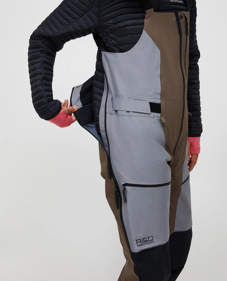 Peak Performance Vertical Gore-Tex Pro Bib Pants för damer i färgerna terrain tan och ljusgrå, där sidan av byxan visas med dragkedja.