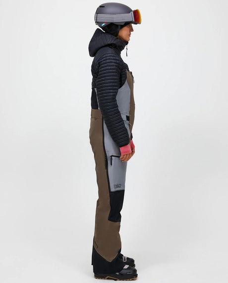 Skidåkare i profil som bär Peak Performance Vertical Gore-Tex Pro Bib Pants för damer i färgerna brun och ljusgrå.