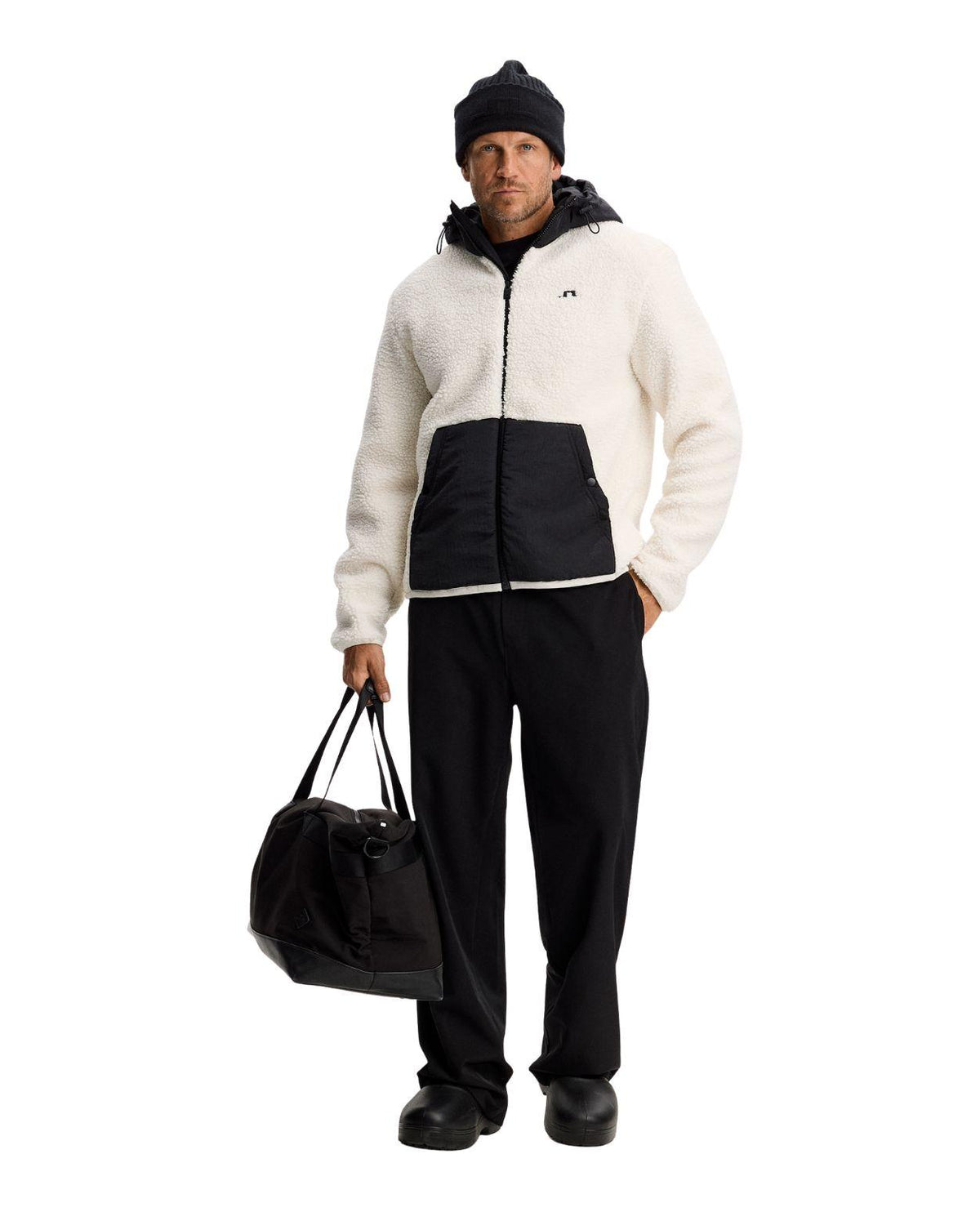 Man i en beige J.Lindeberg Varek Hybrid Zip Hood mellanlagerjacka i fleece med svart huva och väska.