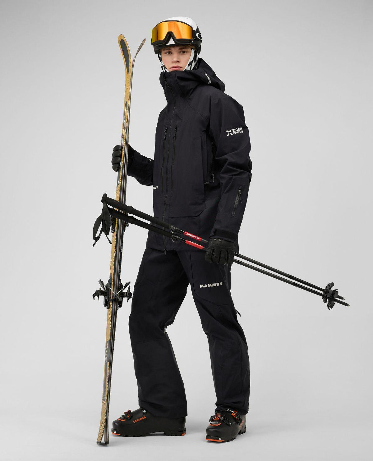 Skidåkare i svart Mammut Eiger Free Pro HS Hooded Jacket med hjälm, skidor och pjäxor.
