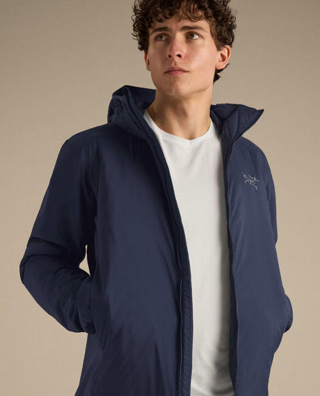 Man i en mörkblå Arc'teryx Atom Hoody med huva och en vit t-shirt under.