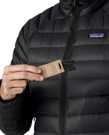 Närbild på person som håller i lagningslappar framför svarta dunjackan Patagonia Down Sweater Women