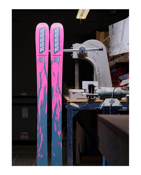 Rosa och blå K2 Mindbender 96 Women allmountainskidor stående i en verkstadsmiljö.