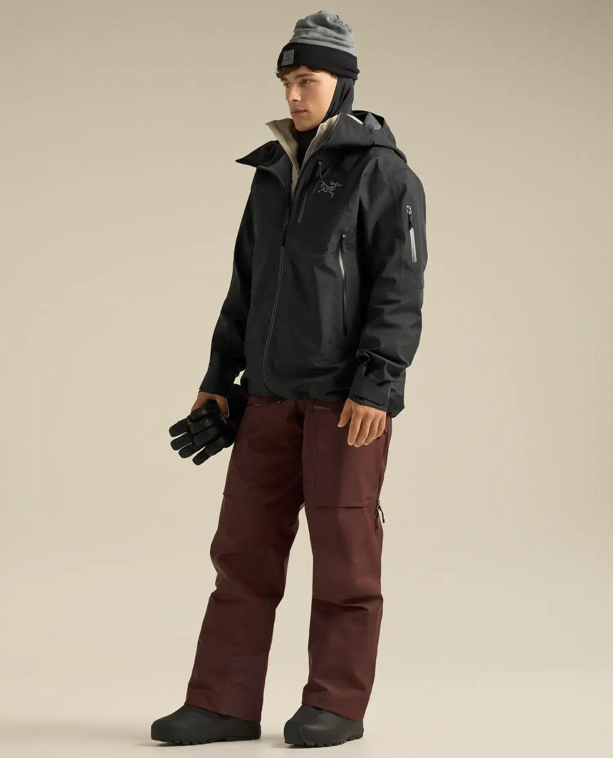 En skidåkare bär Arc'teryx Sabre Jacket Men i svart i en studio med röda skidbyxor.