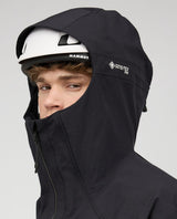 Skidåkare i svart Mammut Eiger Free Pro HS Hooded Jacket med hjälm och huva uppdragen.